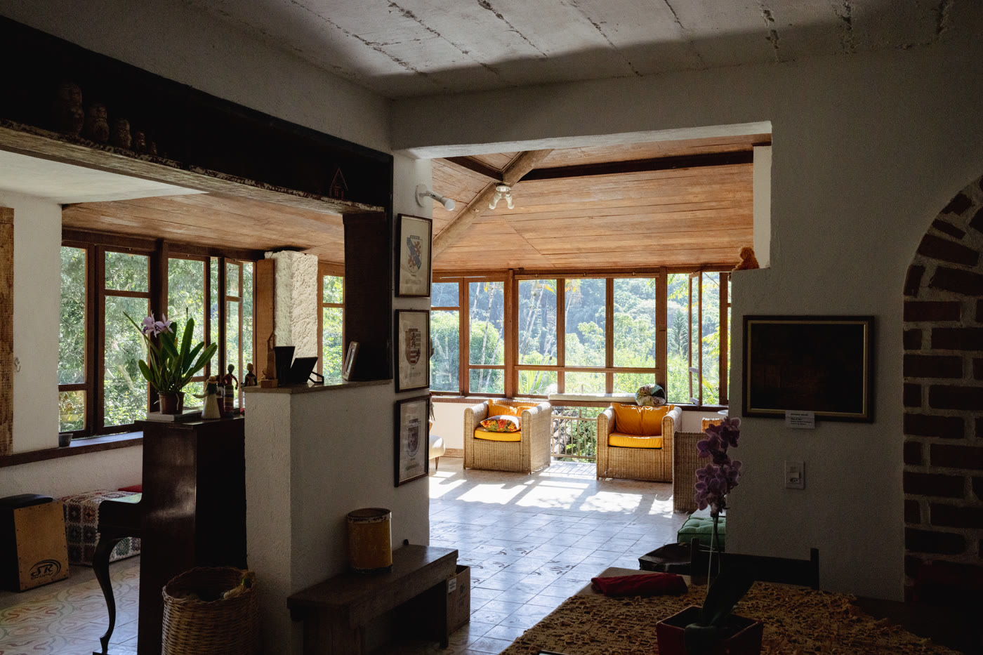 Sala da casa-sede da Fazenda dos Cordeiros, com poltronas de vime, orquídeas floridas e vista para a Mata Atlântica